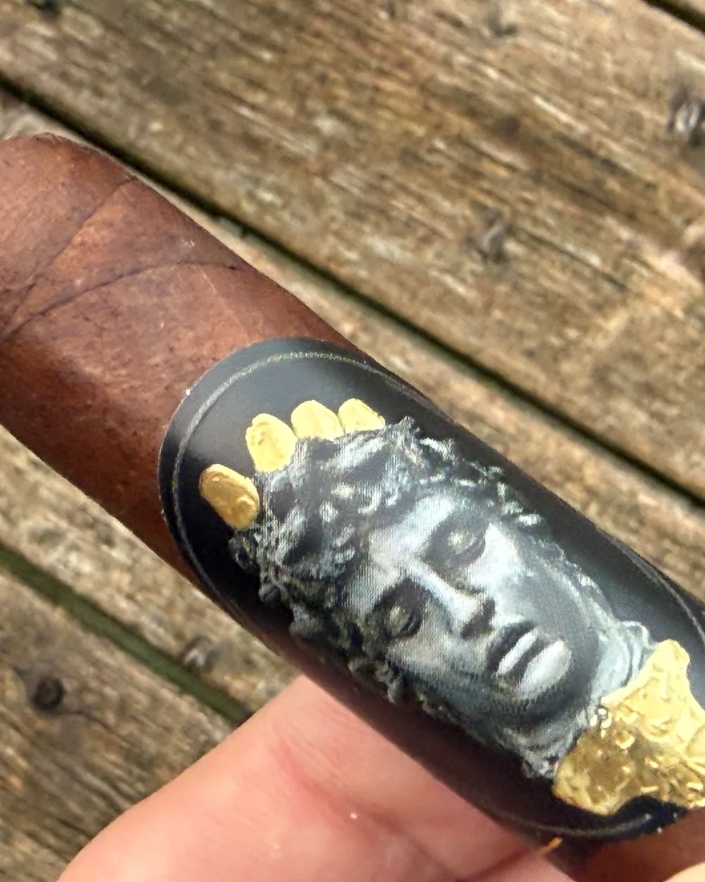 Close-up of the ALEC & BRADLEY GATEKEEPER TORO 6×52 band, the silver Medusa medallion with gold flecks and a gold drip, held on the porch