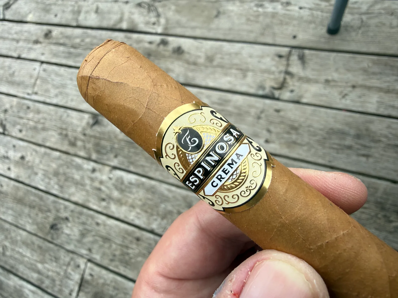 The Espinosa Crema cigar held on the porch, gold and black band in focus