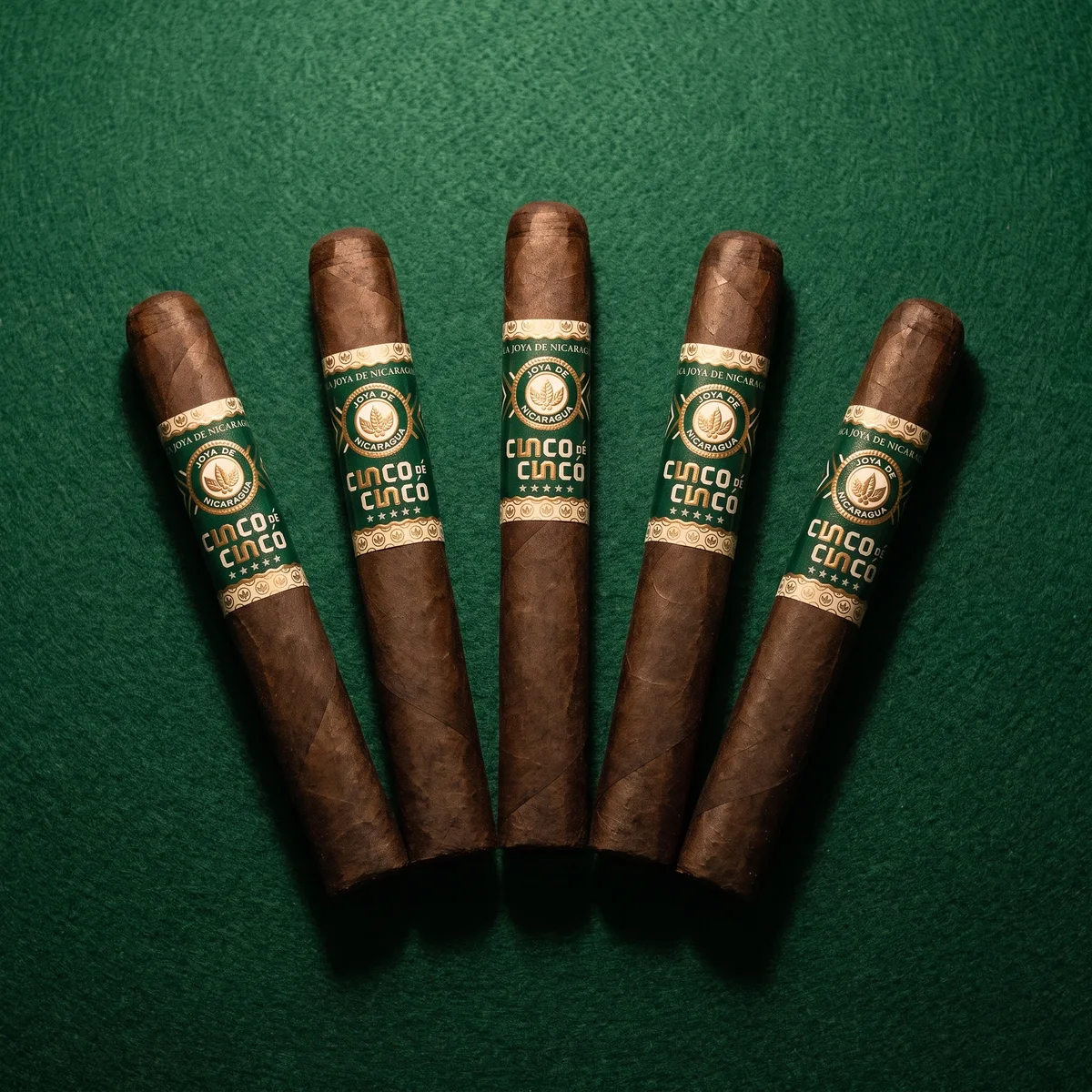 JOYA DE NICARAGUA CINCO DE CINCO TORO 6&times;52 - five cigars fanned on green felt showing the emerald and ivory bands