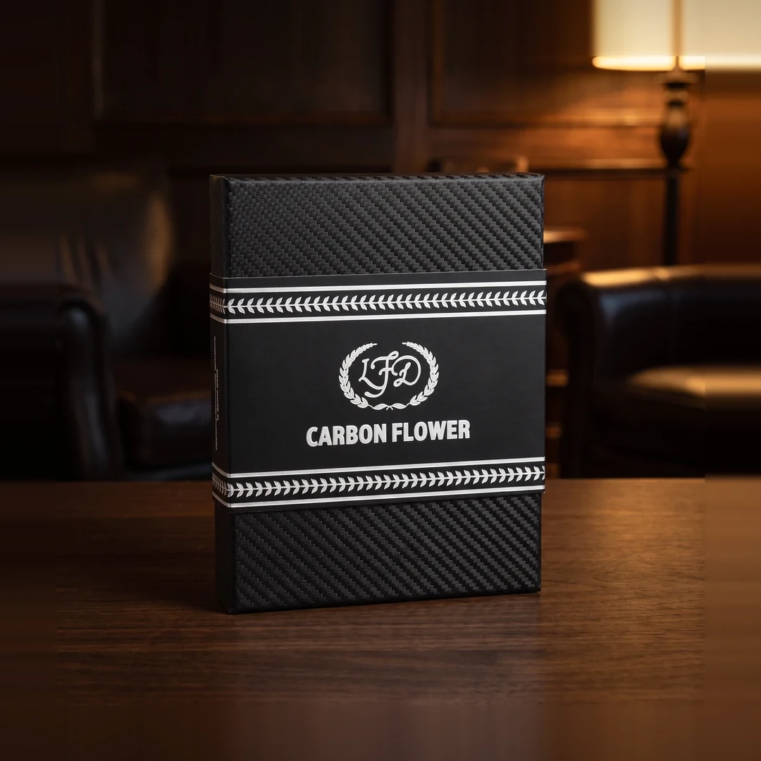 La Flor Dominicana Carbon Flower cigar box standing upright on a table, black carbon fibre twill weave with a white laurel braid band, the LFD monogram in a laurel wreath and CARBON FLOWER in white capitals