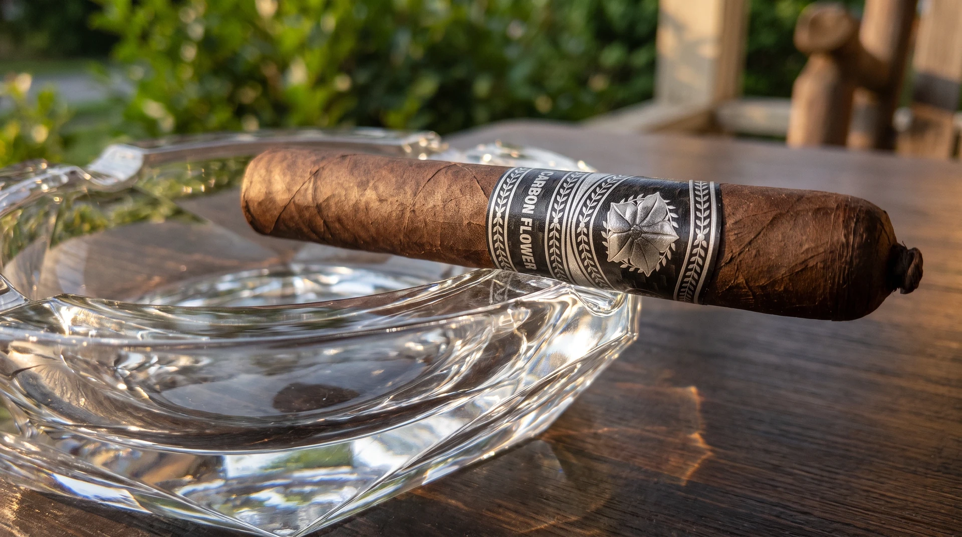 Unlit La Flor Dominicana Carbon Flower cigar resting across a heavy crystal ashtray on a wooden porch table