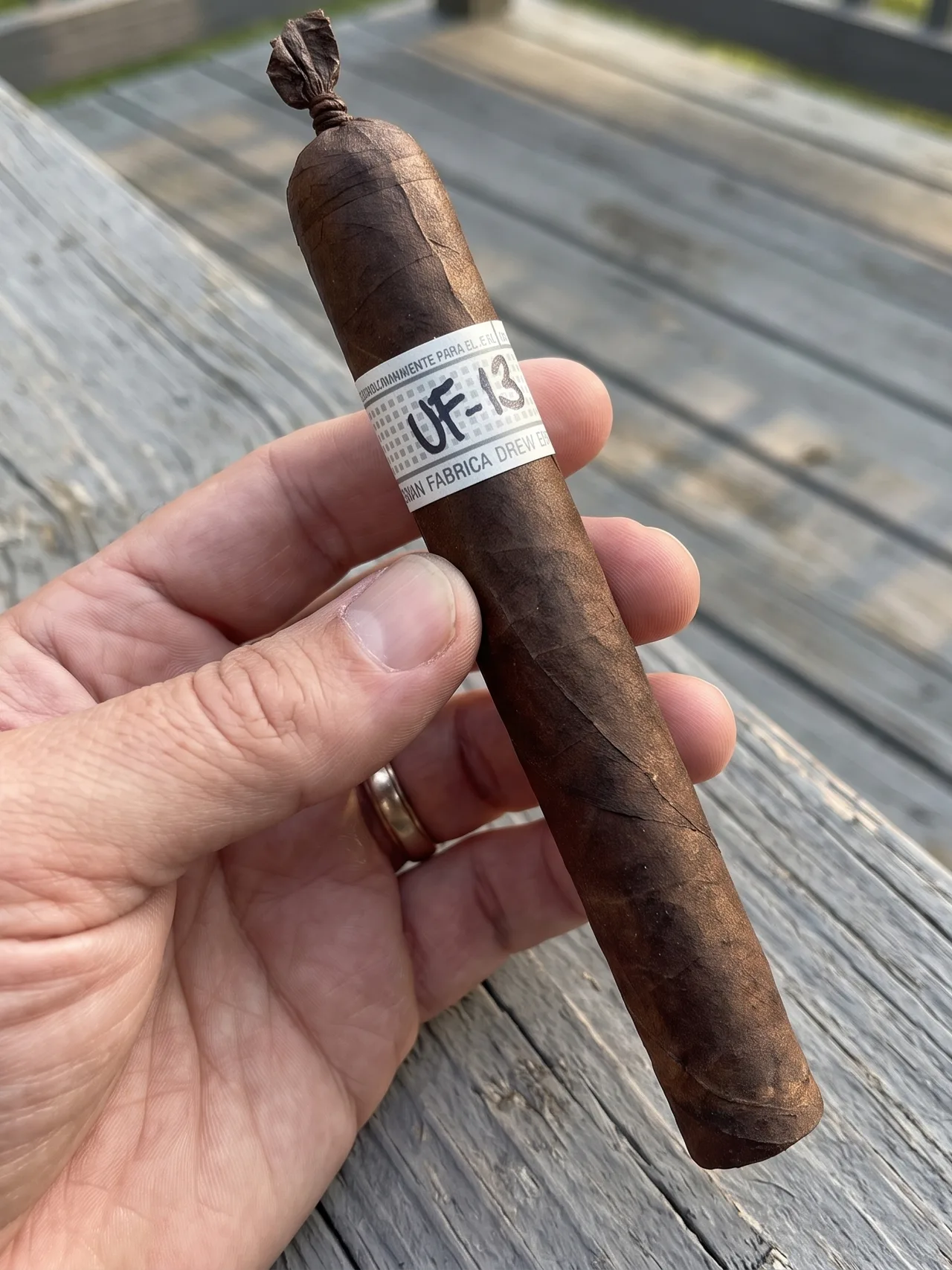 Hand holding the Liga Privada Unico Serie UF-13 on a weathered deck