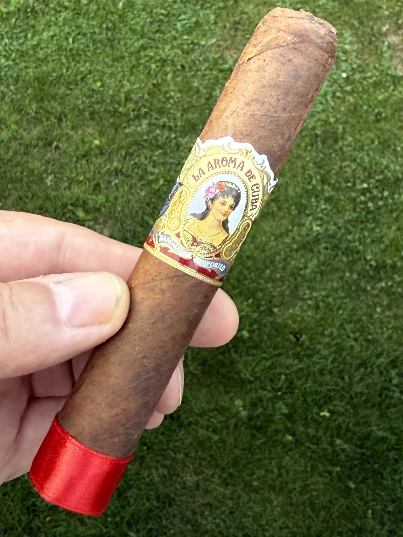 La Aroma de Cuba Robusto held full length, red foot ribbon visible