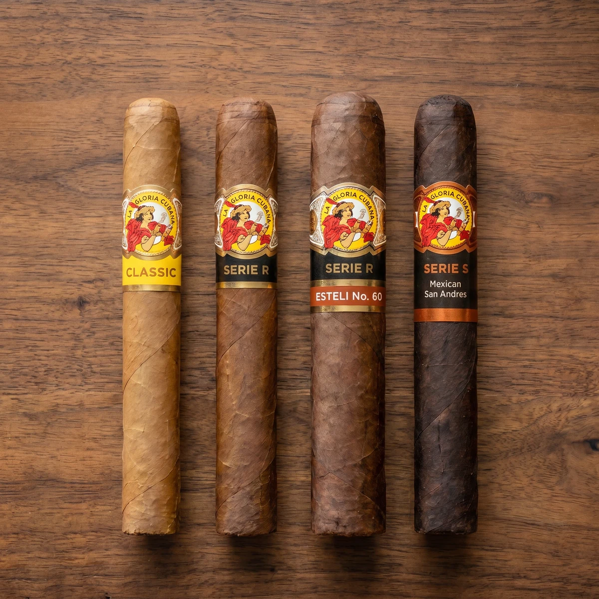 The four La Gloria Cubana blends lying flat in a row on wood, each with its band: the Classic Wavell, Serie R, Serie R Estelí No. 60, and the dark Mexican San Andrés Serie S