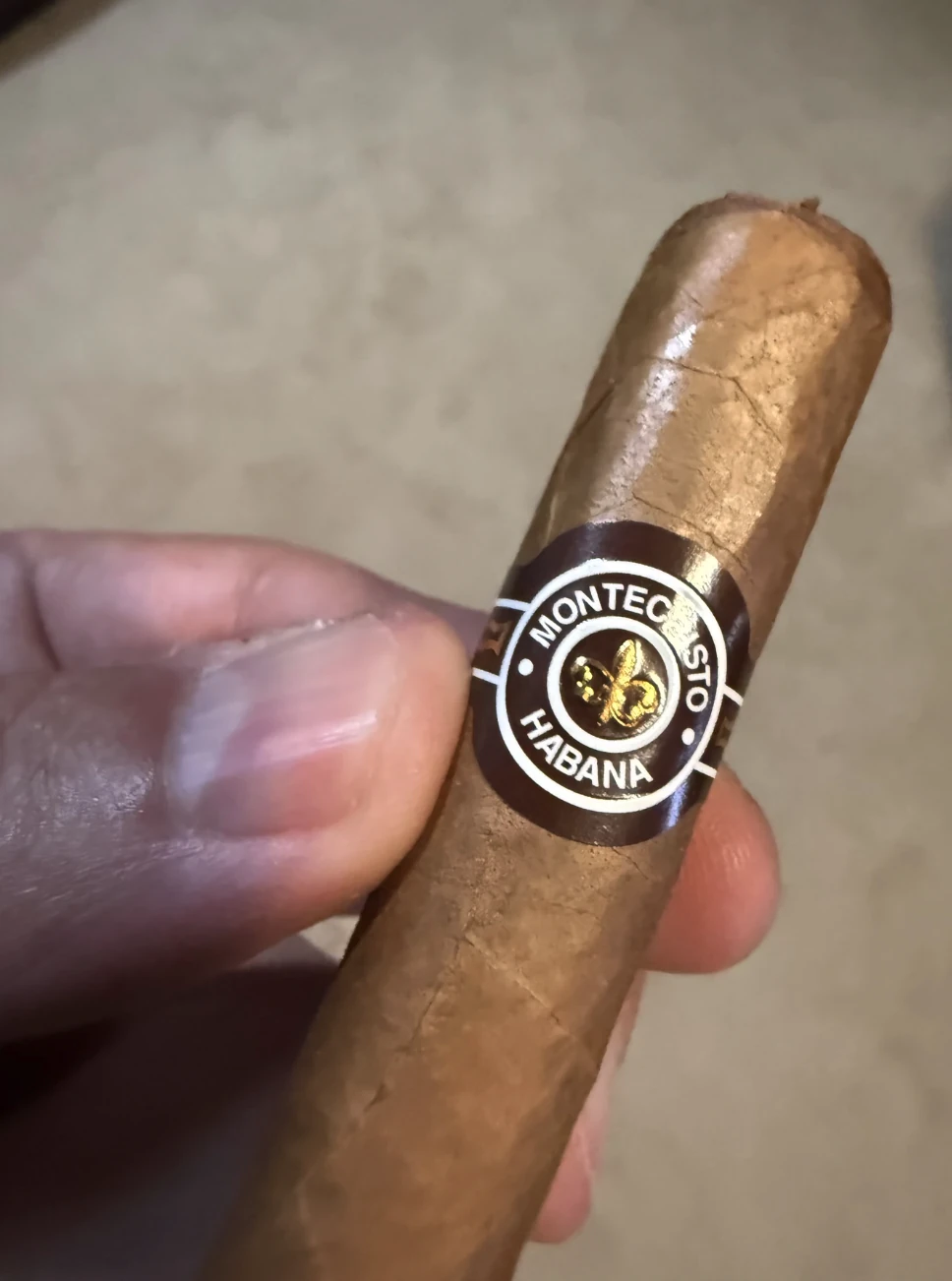 Hand holding a real Cuban Montecristo No. 4 showing the gold fleur-de-lis band up close