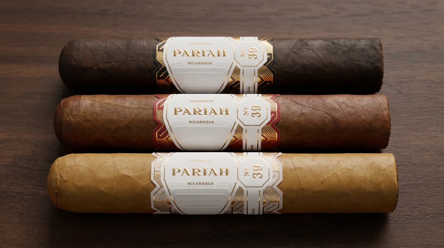 The three Pariah No. 39 cigars lying side by side, each wearing the white-and-gold PARIAH shield band with a black, red, or white accent frame marking its wrapper