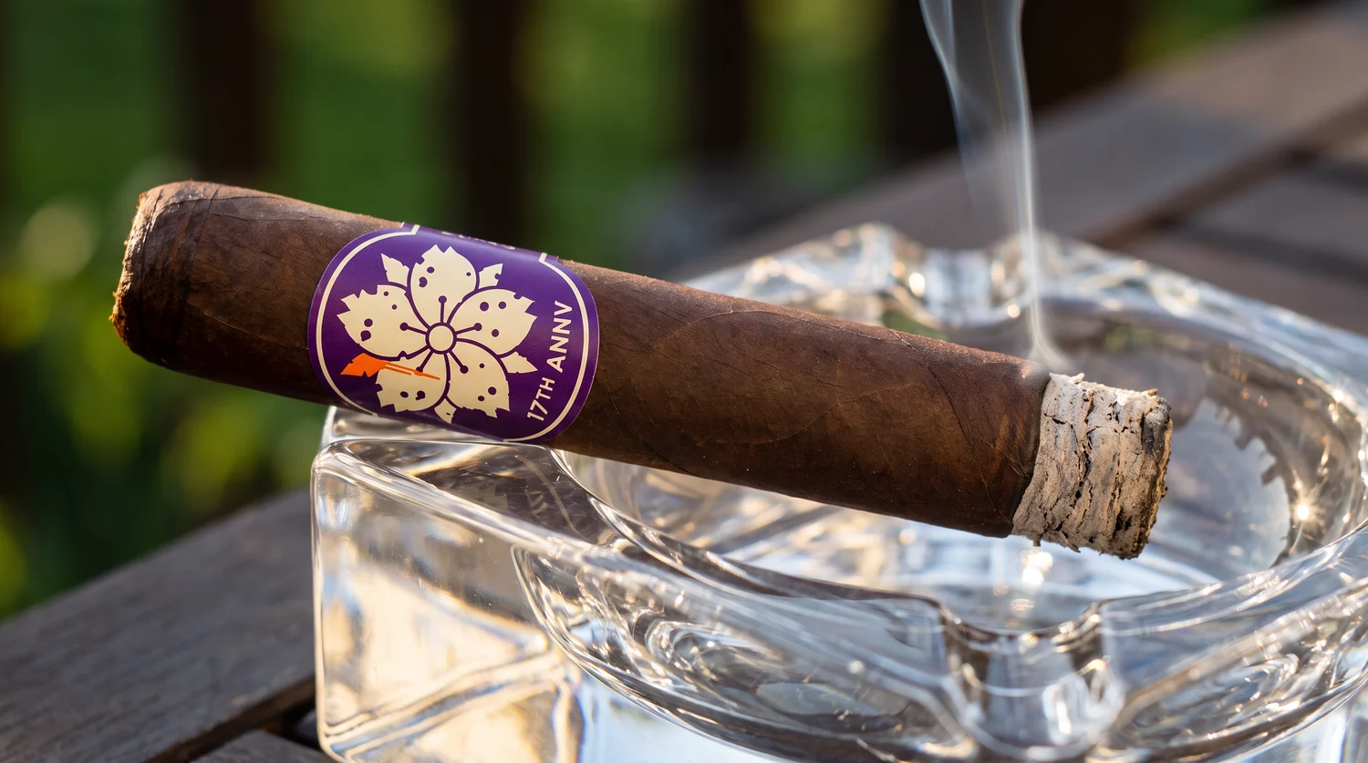 Room101 17th Anniversary cigar resting in a large crystal ashtray, grey ash at the burn line, tall purple 17TH ANNV band facing the camera